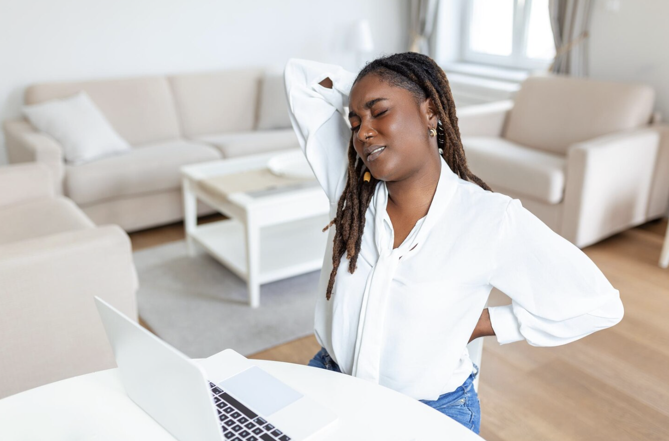 Young woman experiencing neck and back discomfort while working at a desk.