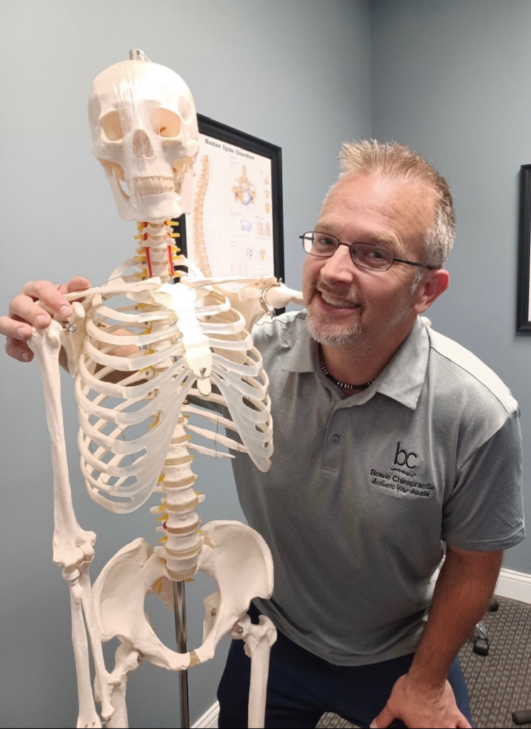 Dr. Bowie smiling beside a chiropractic skeleton model.